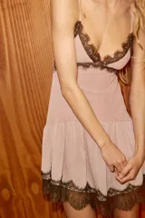 Vestido corto de escote en pico con tirantes finos ajustables, confeccionado en tejido liso con detalles de encaje a contraste en el escote y el ruedo. Presenta un diseño con falda con volado y cierre posterior con cremallera oculta.