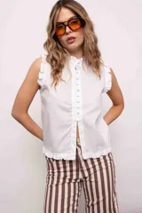Blusa blanca sin mangas con cuello mao y volados en hombros y ruedo. Cierre frontal con botones.