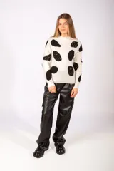 Sweater de punto color blanco con estampado de manchas negras irregulares y detalles de tachas metálicas sobre las mismas. Presenta cuello redondo y puños acanalados.