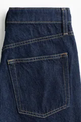 Jean wide leg de tiro alto en denim de algodón rígido color azul oscuro con costuras en contraste de color ocre. Cuenta con diseño de cinco bolsillos y cierre frontal con botón y cremallera.