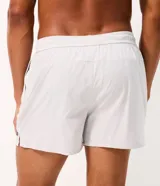Bermuda de running Get Over para hombre, confeccionada en microfibra ligera de color gris claro. Presenta cintura elástica con cordón ajustable, bolsillos funcionales, dobladillo redondeado con aberturas laterales y pequeño parche con logo de la marca en la pierna izquierda.
