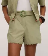 Short de cintura alta confeccionado en cambraia de algodón color verde. Presenta un diseño con ruedo festoneado, trabillas en la cintura y cierre tradicional. Incluye un cinturón al tono con hebilla redonda decorada con pequeños abalorios.