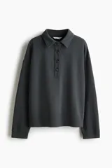 Buzo en tejido liviano color gris oscuro, con cuello camisero, tapeta de botones, hombros caídos y puños acanalados.