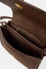 Bolso bandolera de diseño estructurado en color marrón, confeccionado en una combinación de cuero y gamuza. Presenta una solapa frontal con cierre imantado, detalle de tira central con remache metálico y correa larga ajustable para llevar al hombro o cruzado.