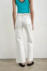 Jeans de denim blanco de tiro alto, corte recto y amplios bolsillos frontales aplicados. Cuenta con cierre frontal abotonado con múltiples botones metálicos a la vista y pespuntes en contraste.