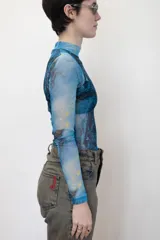 Remera traslúcida de cuello alto y mangas largas, con estampado abstracto en tonos celeste, azul y amarillo.