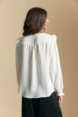 Camisa negra de manga larga con escote en V y cierre frontal de botones. Presenta detalles de volados en los hombros, frunces en la espalda y puños elastizados que le otorgan una silueta relajada y fluida.