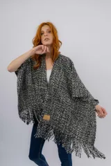 Ruana artesanal tejida en telar manual, con diseño jaspeado en tonos negro y crudo. Presenta una textura rústica y terminación con flecos en el ruedo, además de una etiqueta de cuero con la marca Pura Lana.