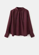 Blusa de manga larga bordó con cuello alto y detalle de fular integrado para anudar al cuello, corte recto y puños abotonados.