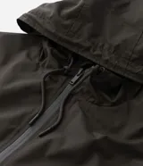 Campera rompevientos de color gris oscuro, con capucha ajustable mediante cordones, cierre frontal por cremallera y bolsillos laterales con cierre. Presenta puños elásticos y un diseño liso y minimalista.