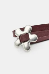 Cinturón de tiras dobles efecto piel en color bordó, con aplicación de piezas metálicas en forma de flores y cierre ajustable mediante nudo.