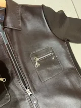 Campera de cuero color chocolate con mangas de lana tejida. Presenta cierre frontal, bolsillos con cierre en el pecho y detalle de ojales metálicos en el ruedo.