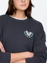 Buzo de cuello redondo en color gris oscuro, con diseño de hombros caídos y puños acanalados. Presenta un pequeño bordado en el pecho con el logo de la marca y dos raquetas de tenis cruzadas.