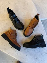 Botas cortas negras de cuero sintético con plataforma y suela track. Presentan dos correas con hebillas doradas y tirador trasero.