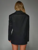 Vestido tipo blazer negro de corte entallado, con solapas clásicas, mangas largas y cierre frontal cruzado con lazo ajustable en la cintura.