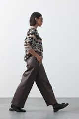 Pantalón de cuero sintético con fit barrel, de silueta amplia con volumen en las piernas y botamanga levemente entallada. Presenta bolsillos laterales y cierre frontal.
