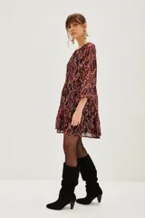 Vestido corto de jacquard con estampado ikat en tonos bordó y detalles metalizados. Presenta mangas largas abullonadas, escote en V con lazo y falda con volados.