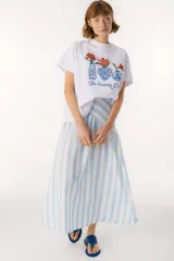 Falda larga color beige de lino, con corte amplio y vuelo, que presenta un canesú diagonal en la parte superior que genera volumen fruncido en la falda.