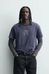 Camiseta de corte relajado con cuello redondo y manga corta. Presenta un acabado con efecto lavado que le otorga una apariencia única y desgastada. Incluye estampados a contraste en la parte frontal.