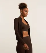 Campera deportiva de corte ajustado, confeccionada en tejido seamless de poliamida y elastano. Presenta cuello alto, cierre frontal con cremallera y textura acanalada.