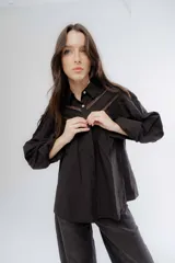 Camisa de algodón color negro con detalles de encaje tipo broderie en el pecho y mangas. Presenta cuello clásico, cierre frontal con botones y mangas largas abullonadas.