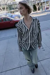 Camisa de cuello solapa con escote pico y manga larga. Presenta un bolsillo delantero de plastrón y bajo con aberturas laterales con cordones ajustables. Cierre frontal con botones.