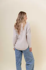 Buzo tejido de punto en color beige, con cuello redondo, mangas largas y silueta relajada con dobladillo irregular, siendo más largo en la parte trasera.