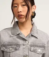 Campera corta de jean color negro con cuello inglés, abotonadura frontal, bolsillos tipo parche con solapa en el pecho y mangas largas.