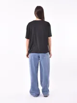 Remera blanca de manga corta con cuello en V y apliques de tachas metálicas doradas dispuestas en forma de V invertida en la zona de los hombros.