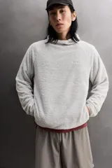 Sudadera regular fit de tejido polar con textura efecto pelo, color gris claro. Cuenta con cuello subido, capucha ajustada, manga larga ranglán, bolsillos laterales en la cadera y bajo asimétrico más largo en la espalda. Los acabados son con cinta elástica.