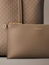 Cartera tote de Calvin Klein en color beige, con estampado de monograma CK repetido en toda la superficie, doble asa fija y diseño estructurado.