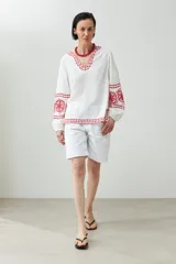 Blusa blanca de lino con bordados rojos en cuello, mangas y ruedo, de corte holgado y manga larga.