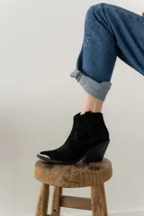 Bota corta de cuero gamuzado color negro, con punta fina y diseño bordado estilo western. Tiene un pequeño tirador en la parte trasera y un taco cónico de altura media.