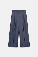 Pantalón ancho de mezclilla azul oscuro, tiro medio, con pinzas delanteras y pespuntes a contraste. Presenta cierre frontal con botón y cremallera.