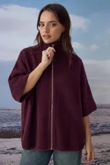 Poncho tejido color bordó con cuello alto y cierre frontal completo. Presenta mangas cortas con terminación en puño acanalado y un diseño holgado.