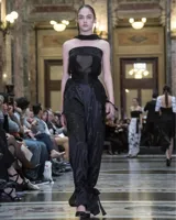 Pantalones de lúrex negros, de tiro alto con detalle de tableados en el frente, lazo detrás y cintas a la altura de los tobillos para ajuste.