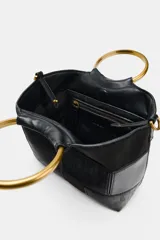 Bolso tipo saca en formato mini con diseño de patchwork en tonos marrones. Cuenta con una anilla metálica rígida como asa de mano y una correa bandolera extraíble. El cierre principal es mediante imán e incluye un bolsillo interior con cremallera.
