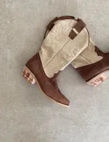 Botas de cuero color marrón y blanco con bordados negros, de estilo cowboy con taco bajo.