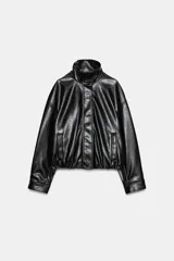 Chaqueta de cuero sintético negro con cuello alto, cierre frontal de cremallera oculto por solapa con botones a presión, mangas largas y bolsillos laterales. Diseño con volumen y bajo elástico.