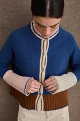 Cardigan de punto con diseño color block en tonos bordó, verde oliva y beige. Presenta cuello redondo con detalle en celeste, cierre frontal con botones y puños acampanados en color beige.