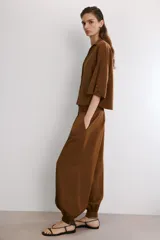 Pantalón de tiro alto en color beige, con diseño de pierna holgada y puños elásticos con cierre de botón en el bajo. Presenta cierre frontal con cremallera y doble botón en la cintura, además de bolsillos laterales.