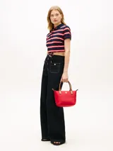 Cartera tote Tommy Hilfiger de nailon rojo, con dos asas superiores en tono tostado y una correa de mano o hombro tejida extraíble. Cuenta con cierre de cremallera superior, compartimento principal e insignia metálica con el monograma TH en el frente.