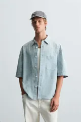 Camisa de corte relajado confeccionada en tejido de algodón, con estampado de cuadros pequeños en tonos celestes y blancos. Presenta cuello solapa, manga corta y bolsillo plastrón en el pecho con cierre frontal de botones.