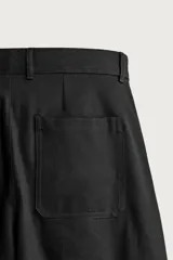Pantalón relaxed fit de algodón color negro, con pliegues frontales en la cintura, bolsillos laterales y cierre frontal con cremallera y botón.