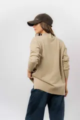 Sweater de tejido de punto color marrón, con cuello alto, corte relajado y terminaciones en rib en puños y cintura. Presenta una hilera de botones metálicos decorativos en uno de los laterales.