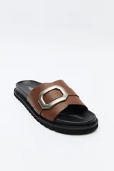 Sandalia slide color beige con hebilla metálica plateada y suela negra.