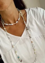 Collar largo de diseño artesanal compuesto por cuentas de vidrio de diversas formas y tamaños, con predominio de tonos claros, blancos y detalles en celeste.