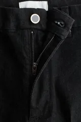 Jean de tiro alto con corte acampanado desde la rodilla, confeccionado en denim suave con leve elasticidad. Presenta cierre frontal con botón, bolsillos traseros insertados y costura central marcada en las piernas.