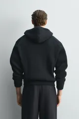 Chaqueta de punto compacto con capucha, confeccionada en hilatura con lana. Presenta cierre frontal con cremallera, mangas largas y acabados en rib.