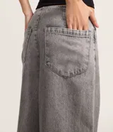 Pantalón de jean gris de tiro bajo y corte amplio, sin pretina, con cierre tradicional y bolsillos.